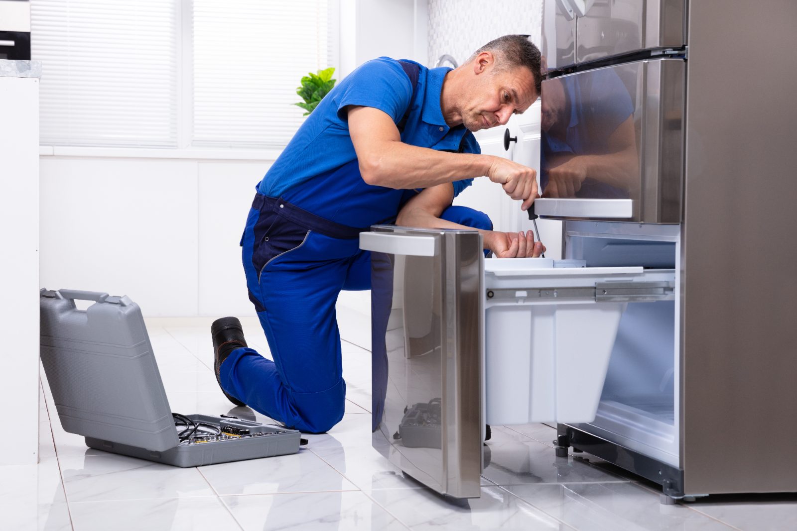 Technician in blue uniform repairing refrigerator in kitchen