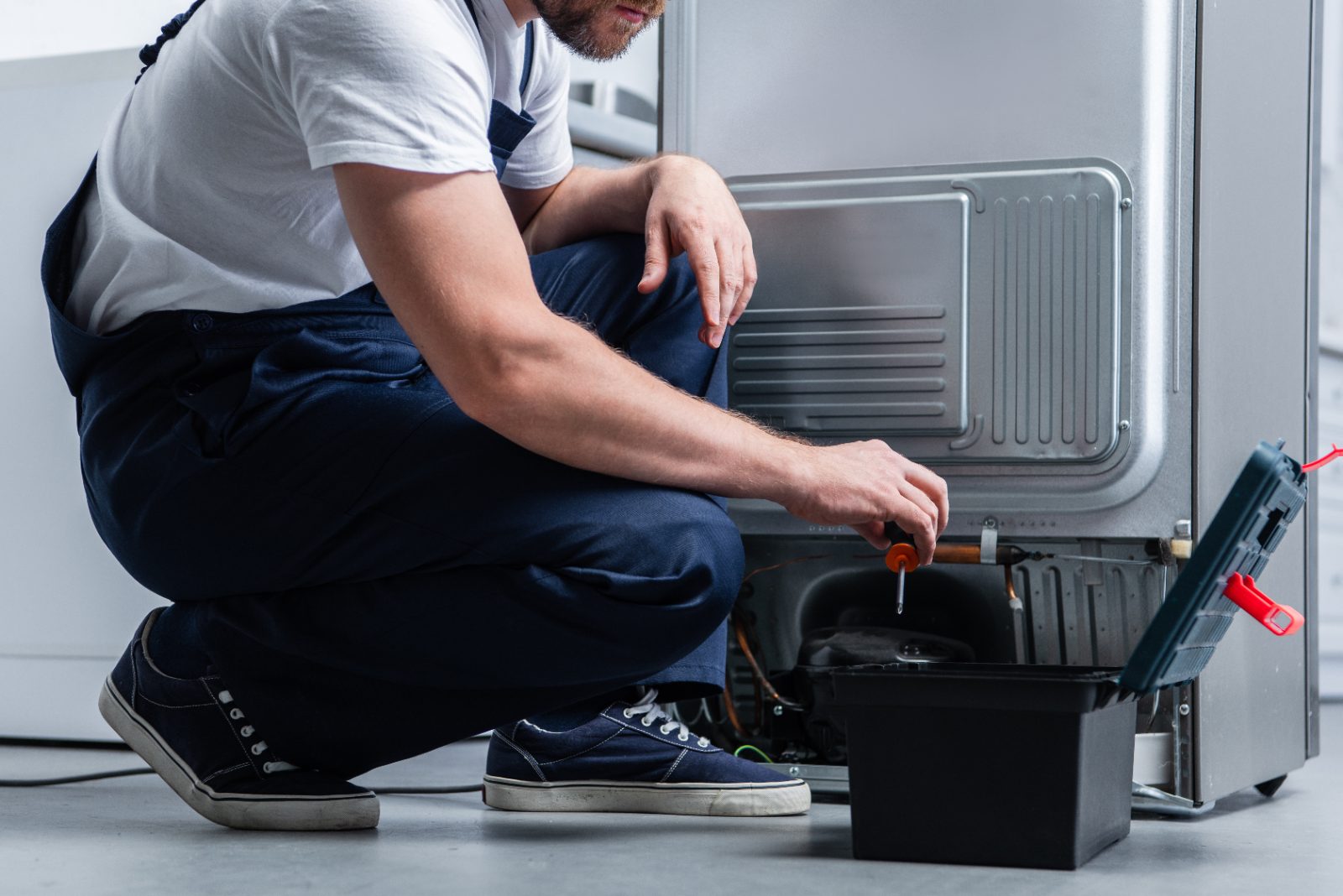 Technician crouching while repairing an appliance with a screwdriver and toolbox